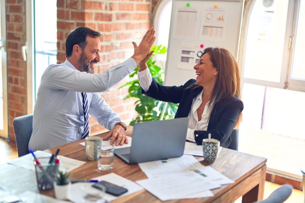 A business woman and man happily high fiving in a meeting. 